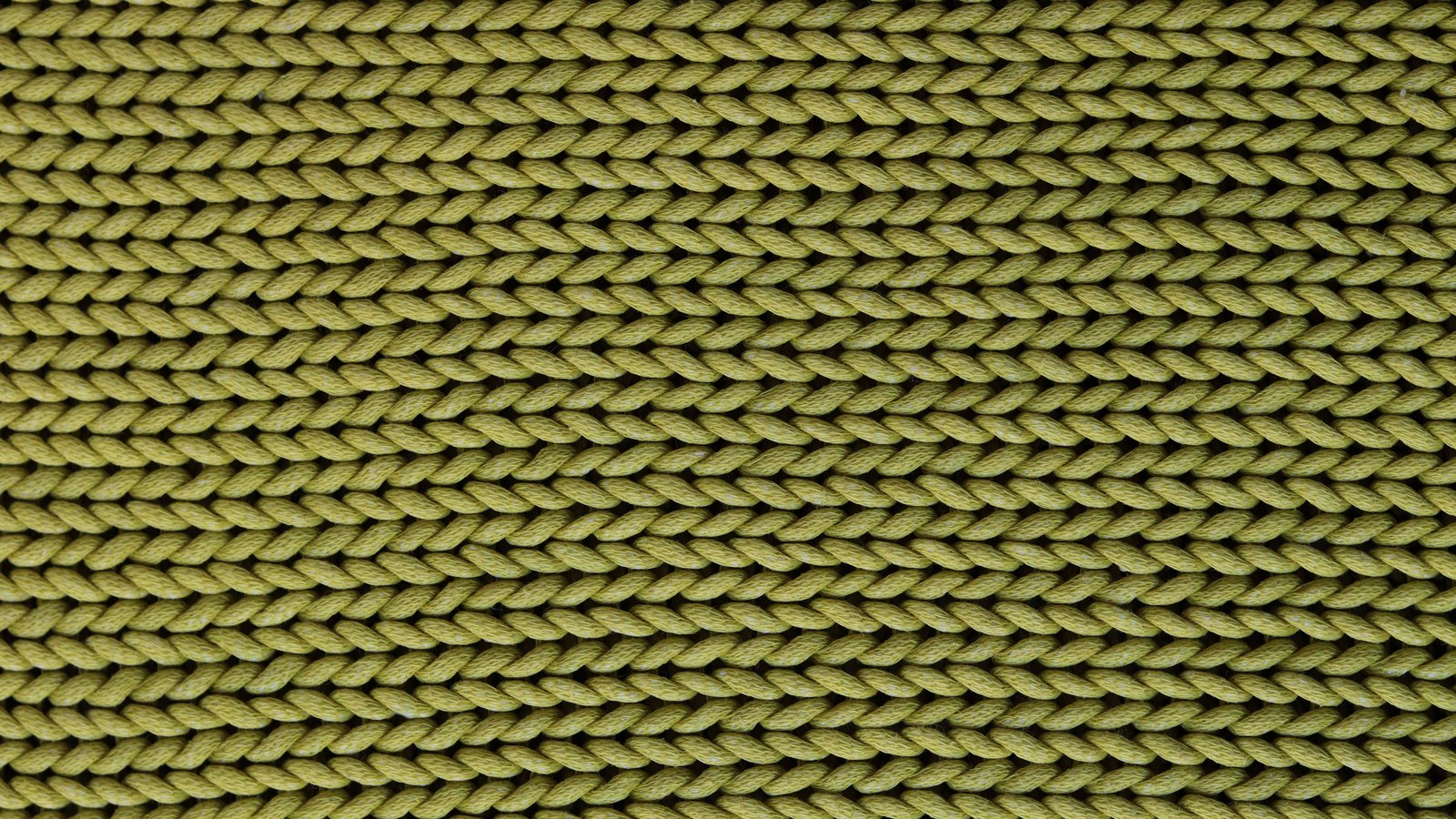 A flat expanse of olive green knitted fabric photographed square on, filling the frame with even horizontal rows of interlocking V-shaped stitches.