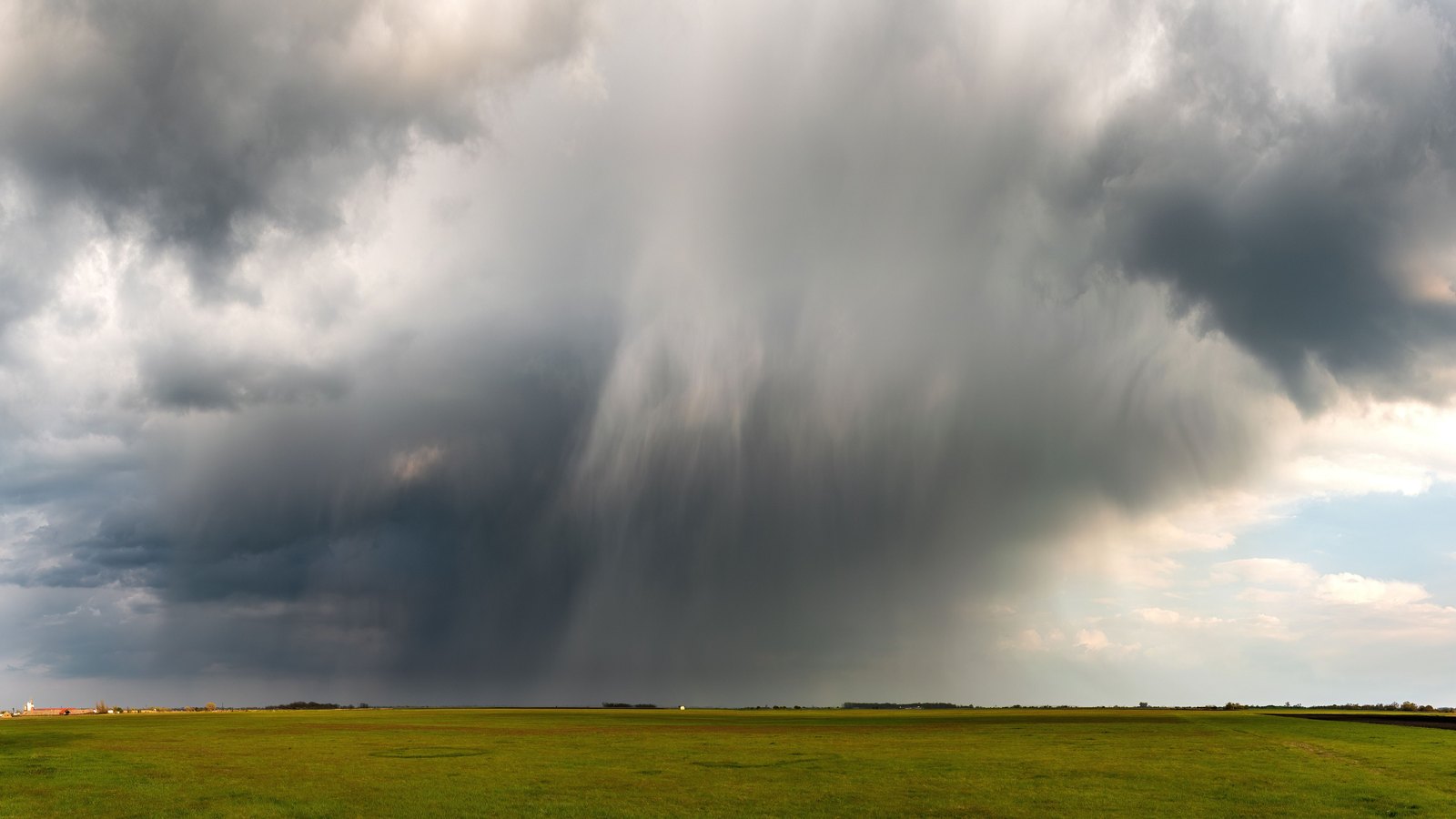 A rain shaft descends from dark storm clouds over a flat field, not a photograph of this event.