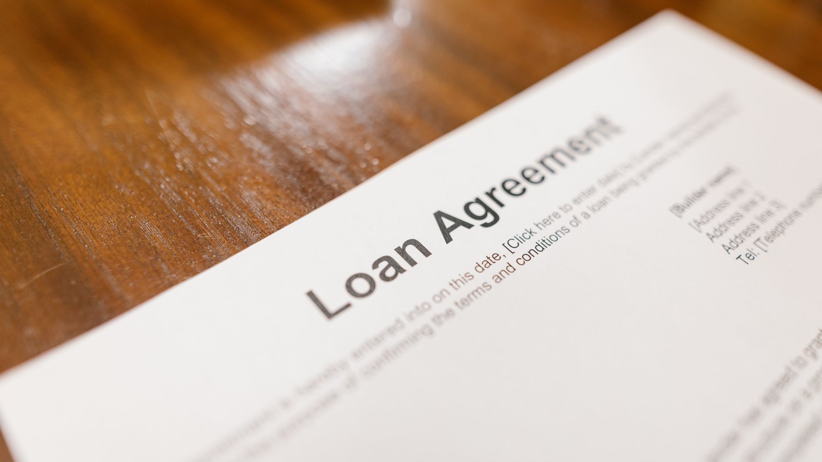 A printed blank loan agreement lying at an angle on a scratched wooden table, its heading legible and every field below it still showing an unfilled bracketed placeholder.
