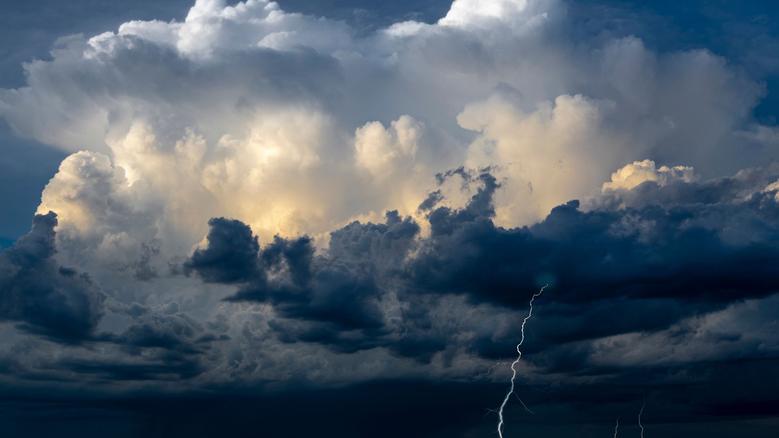 A towering cumulonimbus storm cloud rises over open ocean under a dark sky, with a single lightning bolt striking the water on the right and no land, vessel, person, structure, signage or marking anywhere in the frame. A generic illustration of the kind of deep convection the tropics produce over open water, not a photograph of this event.