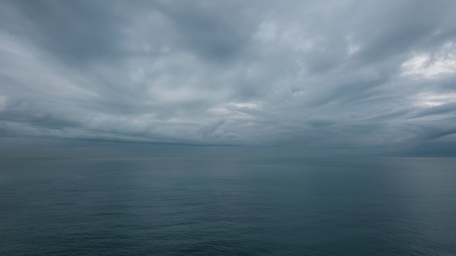 A flat grey-green ocean stretching to the horizon under a low deck of layered storm cloud, the light dim and even. There is no land, no vessel, no person, no signage and no legible text anywhere in the frame, and nothing in it identifies a place. A generic illustration of unsettled weather over open ocean, not a photograph of this event.