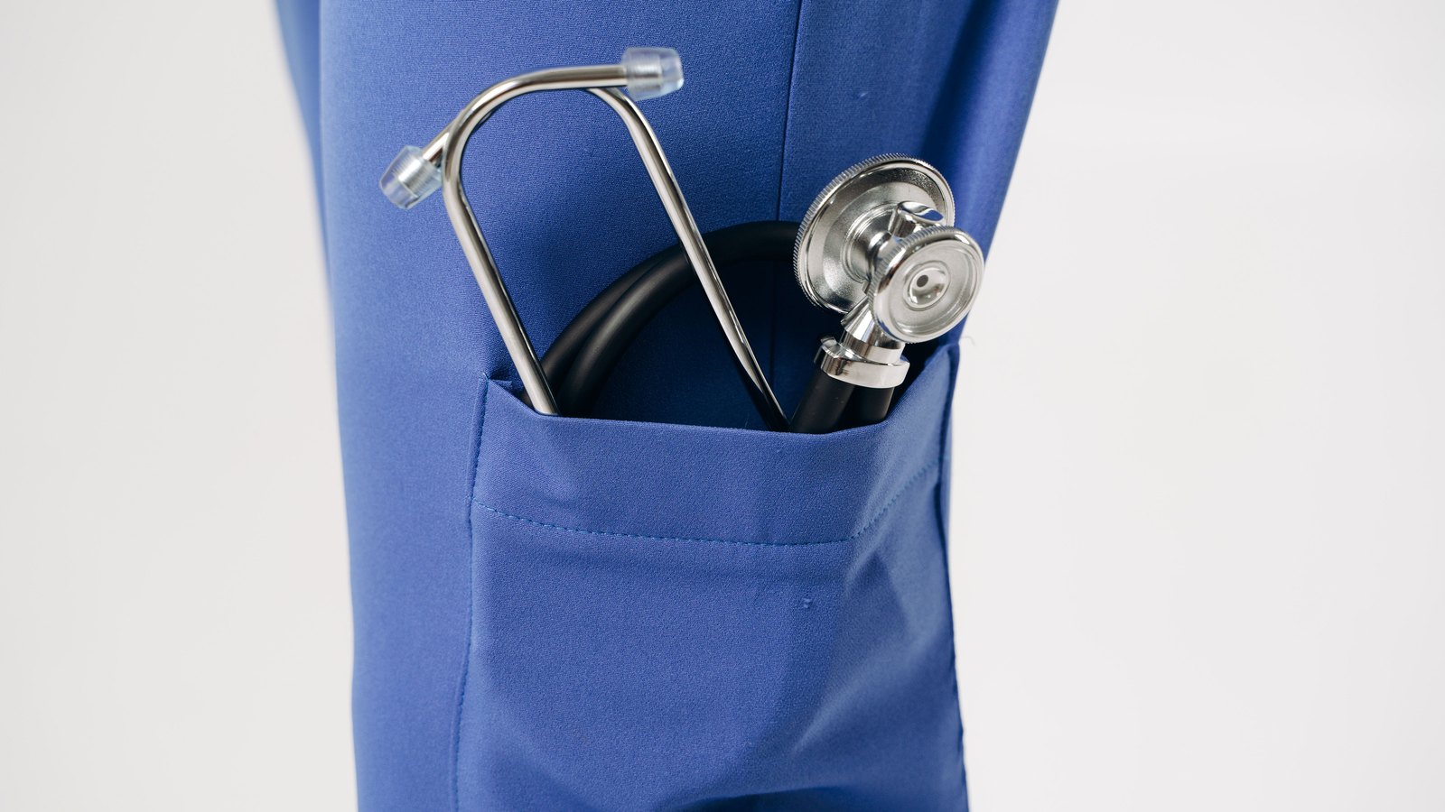 A metal stethoscope tucked into the pocket of blue medical scrubs.