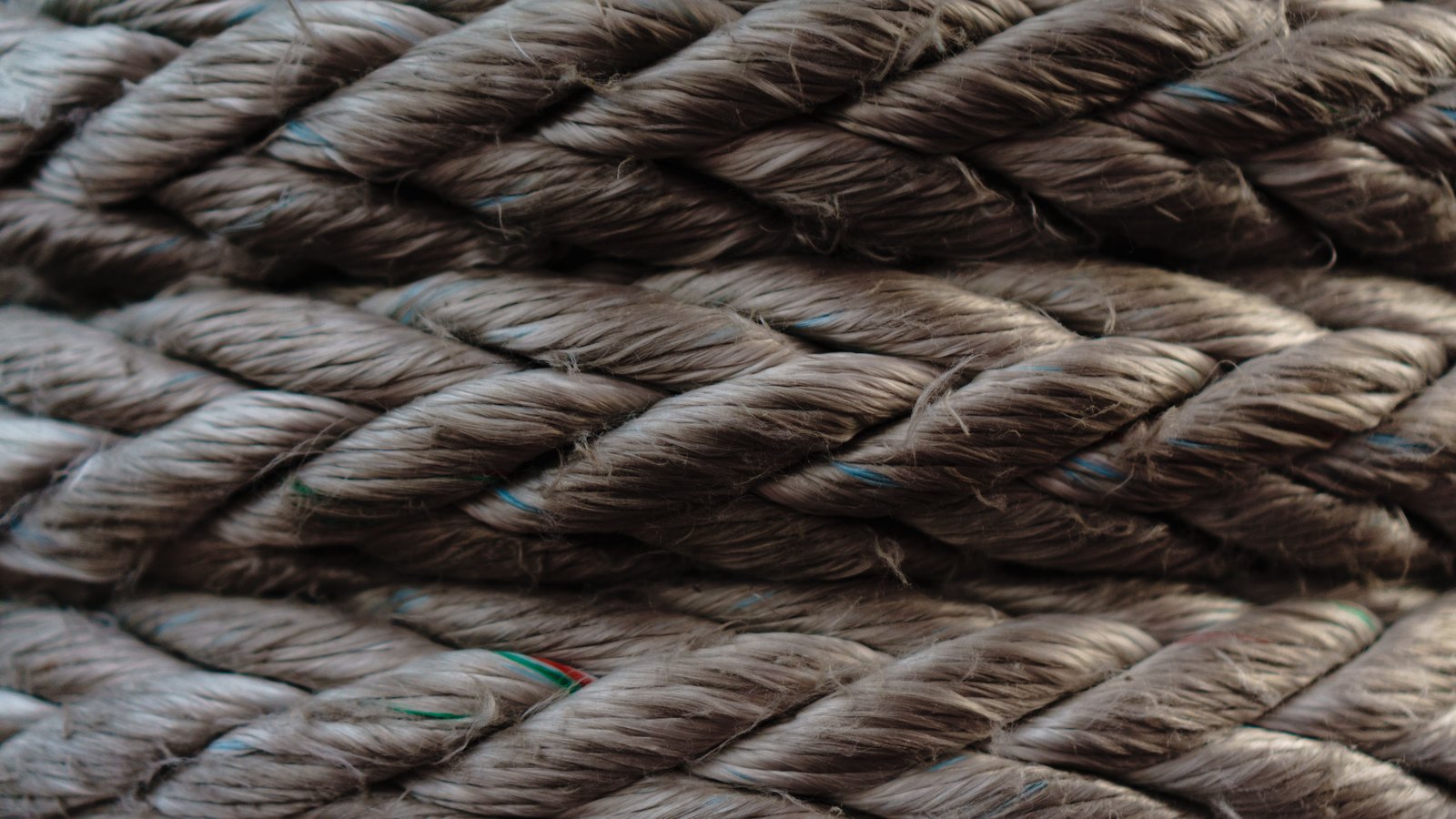 Close macro of heavy three-strand natural fibre rope filling the frame, with a few coloured tracer threads twisted through the strands.