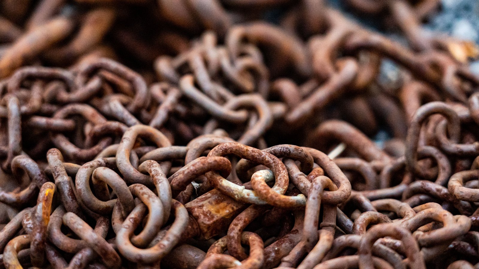 Close macro of a heaped pile of heavy rusted chain, links overlapping in orange and brown, with no vessel or setting visible.