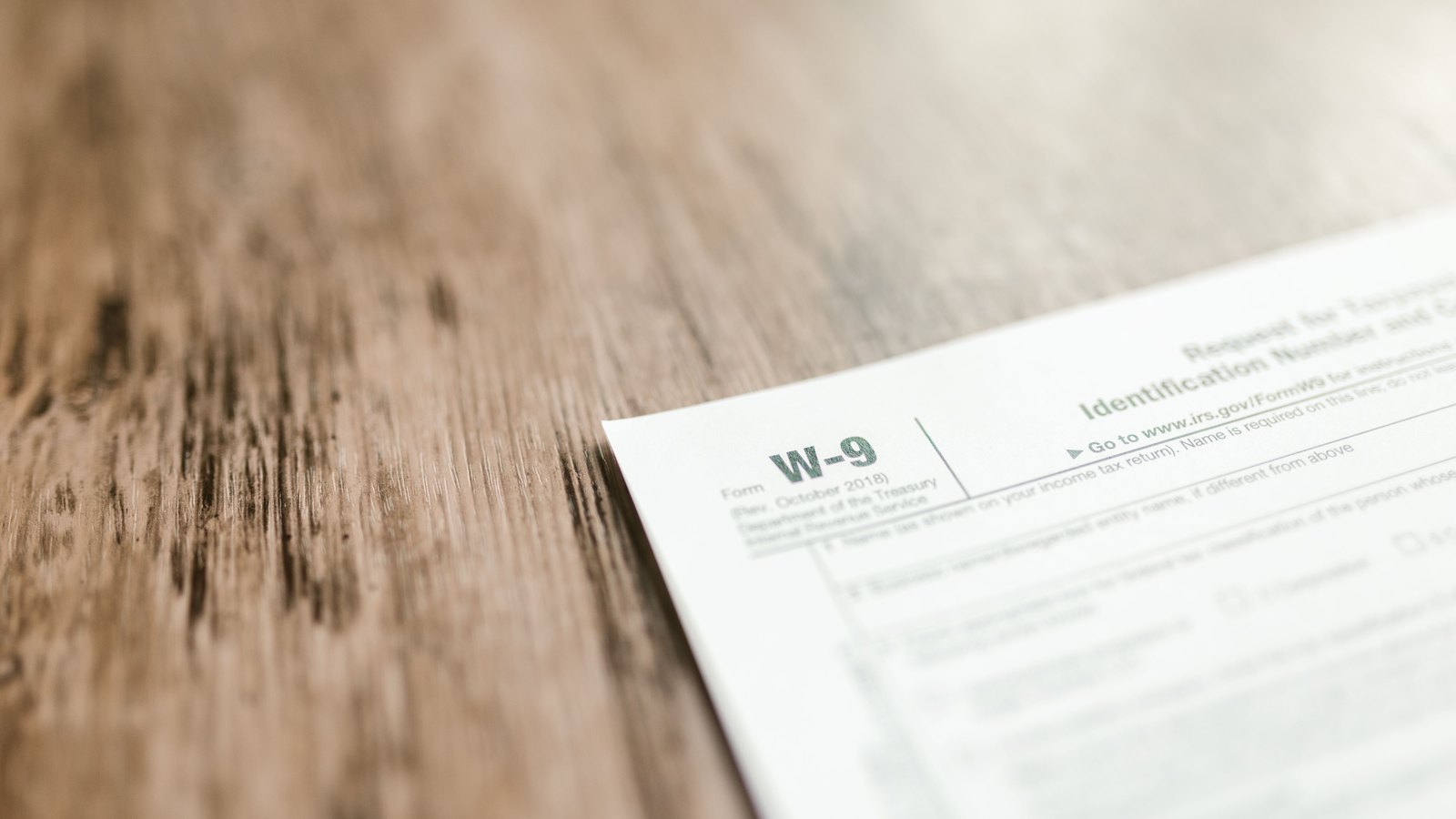 A blank Internal Revenue Service Form W-9, Request for Taxpayer Identification Number and Certification, revised October 2018, lying at an angle on a bare wooden table. Every field is empty and no personal details appear anywhere on it.