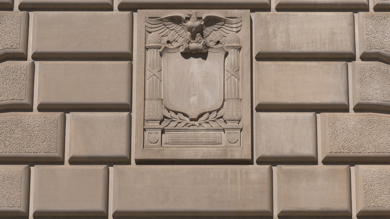 A carved stone eagle above a blank shield, flanked by fasces and set into the rusticated limestone wall of the Internal Revenue Service building in Washington.