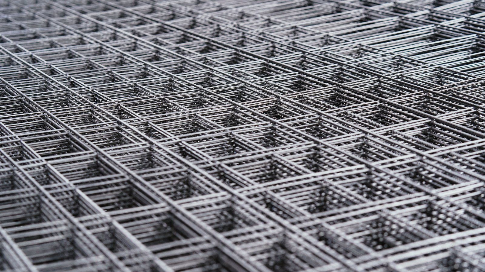Sheets of welded steel reinforcing mesh stacked flat, their square grids overlapping slightly out of alignment and receding across the whole frame.