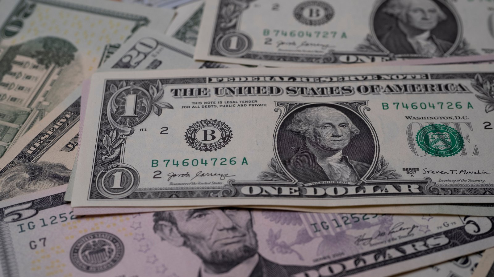United States banknotes lying face up and overlapping, with a one dollar Federal Reserve note on top of twenty, ten and five dollar notes. Nothing else is in the frame.