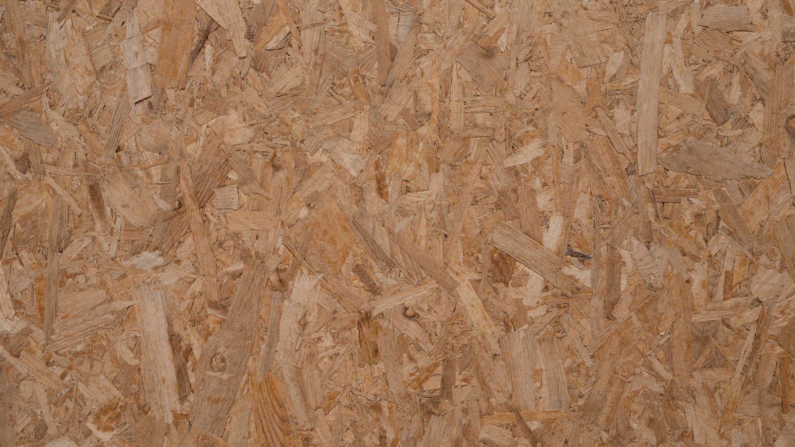 A flat overhead view of an oriented strand board panel, pale tan wood flakes of varying size pressed and glued into a continuous surface that fills the frame. No text, lettering, brand mark, tool, person or place is in view.