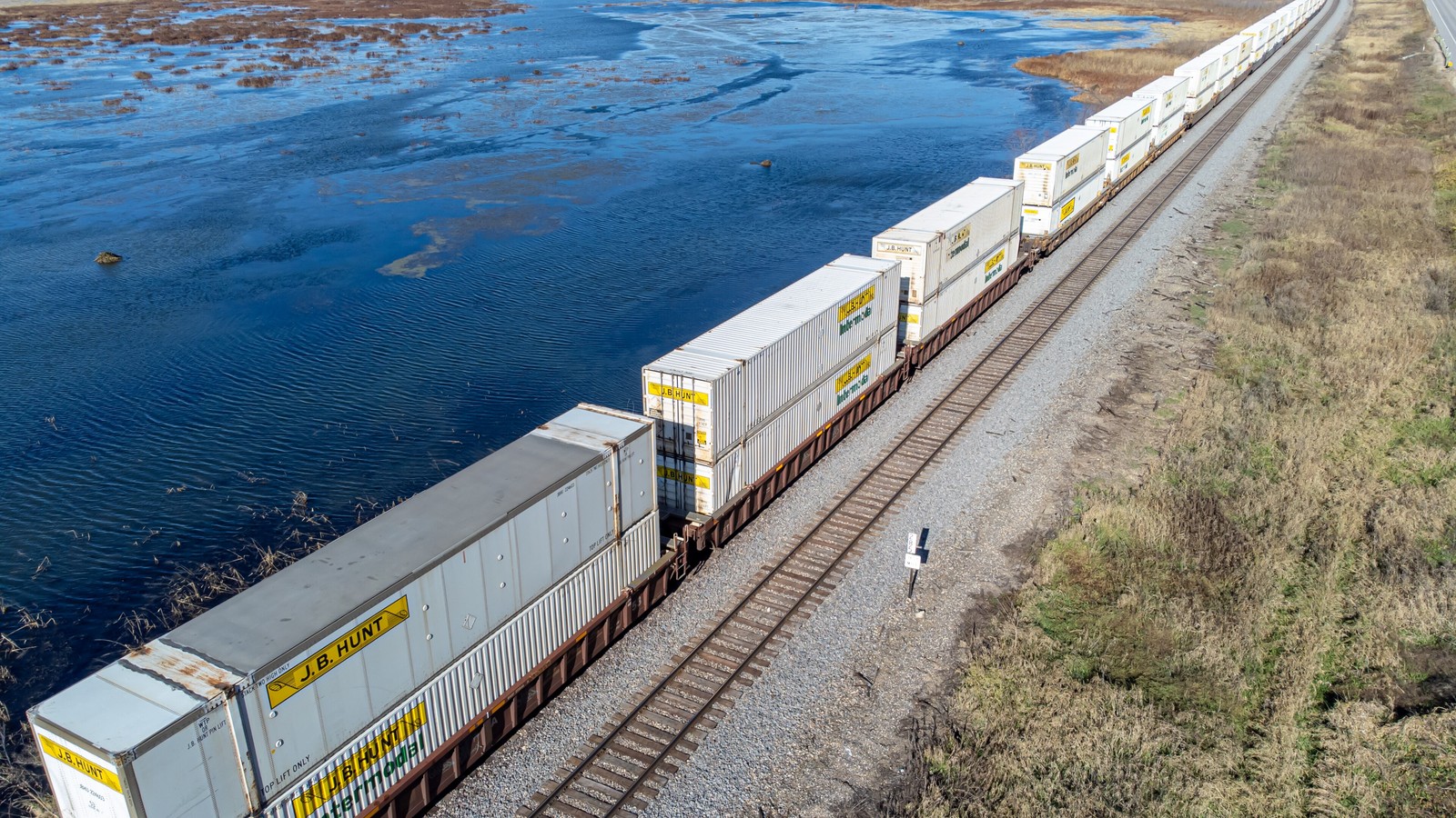 Double-stacked J.B. Hunt containers on a freight train beside water south of La Crosse, photographed in November 2023.