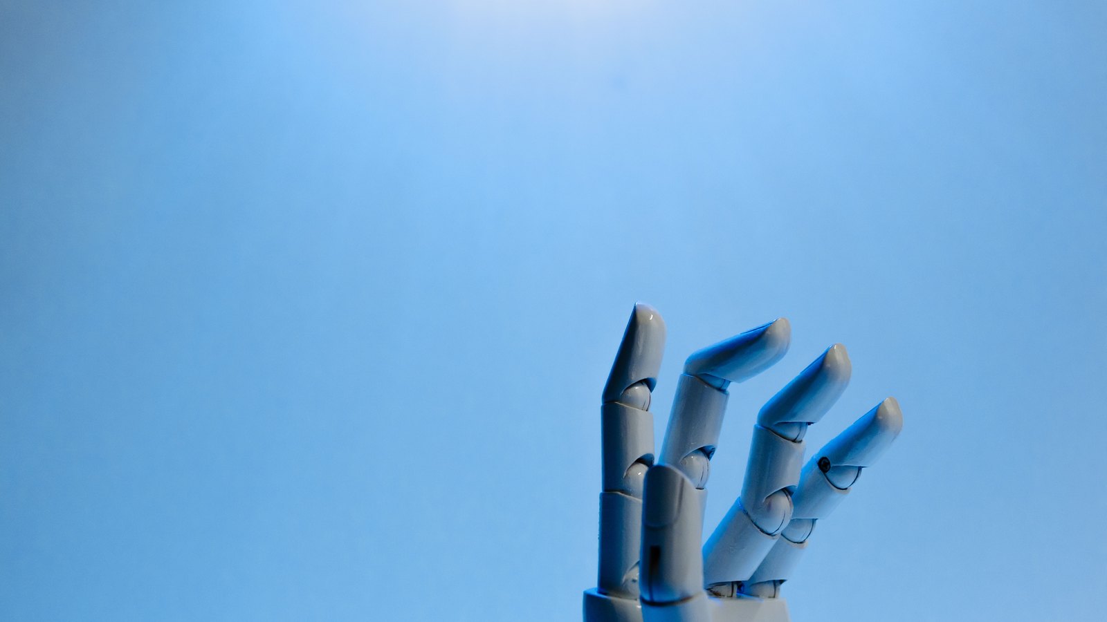 A white articulated robotic hand raised against a plain blue background, its four fingers and thumb curled open, with visible joint pins and moulding seams and no markings on any surface.