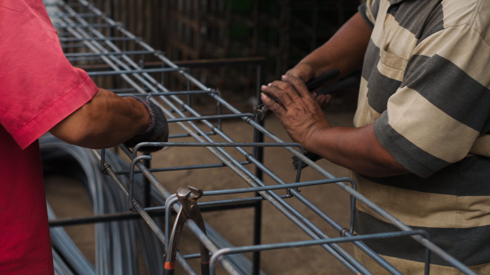 Hands fastening reinforcing steel bars into a rectangular cage.