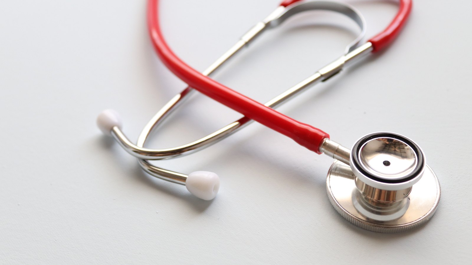 A red stethoscope resting on a white surface.