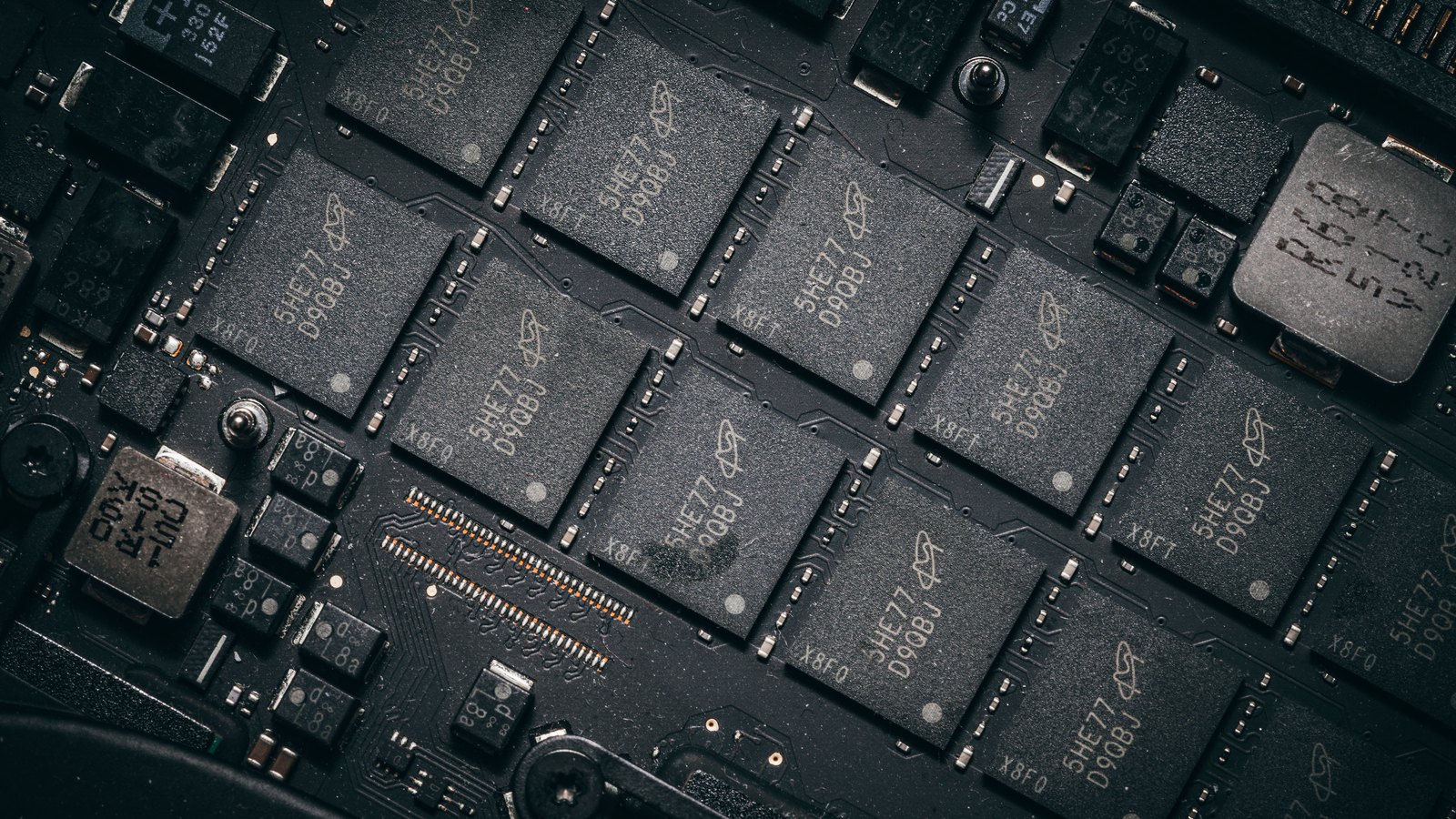 A close grid of black memory chip packages soldered to a dark circuit board, each stamped with pale part codes, filling the frame.