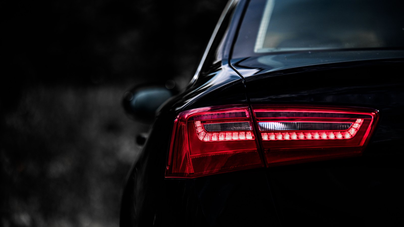 The tail light of a dark car glowing red at night, the rest of the vehicle lost in shadow. Stock photo, not a photograph of this event.