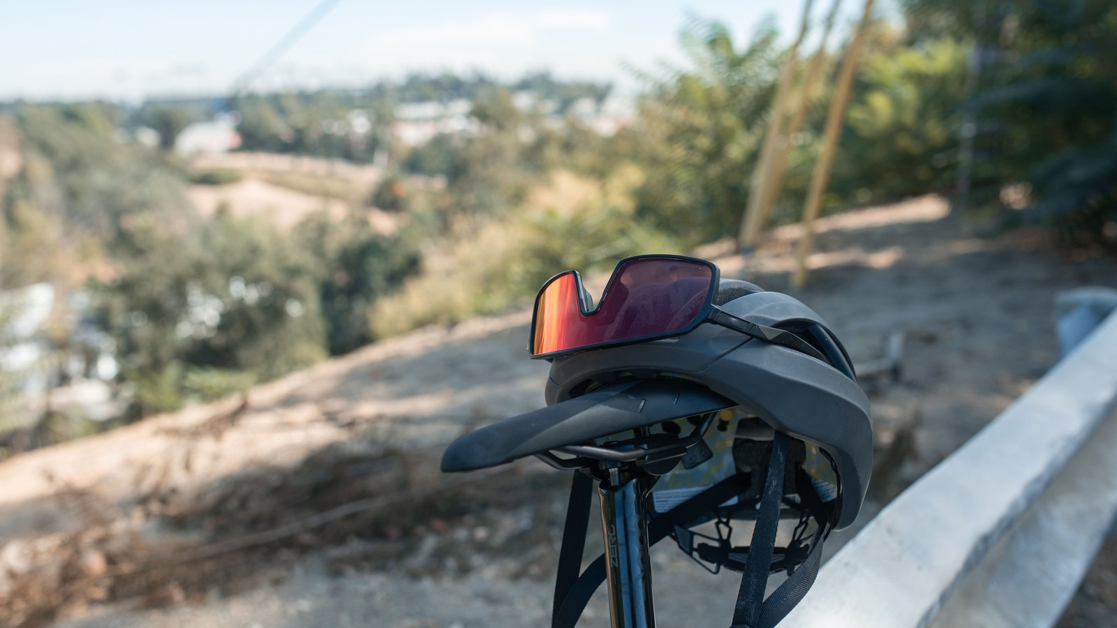 A cycling helmet and sunglasses resting on a road bicycle saddle at the edge of a road, the background thrown out of focus. Stock photo, not a photograph of this event.