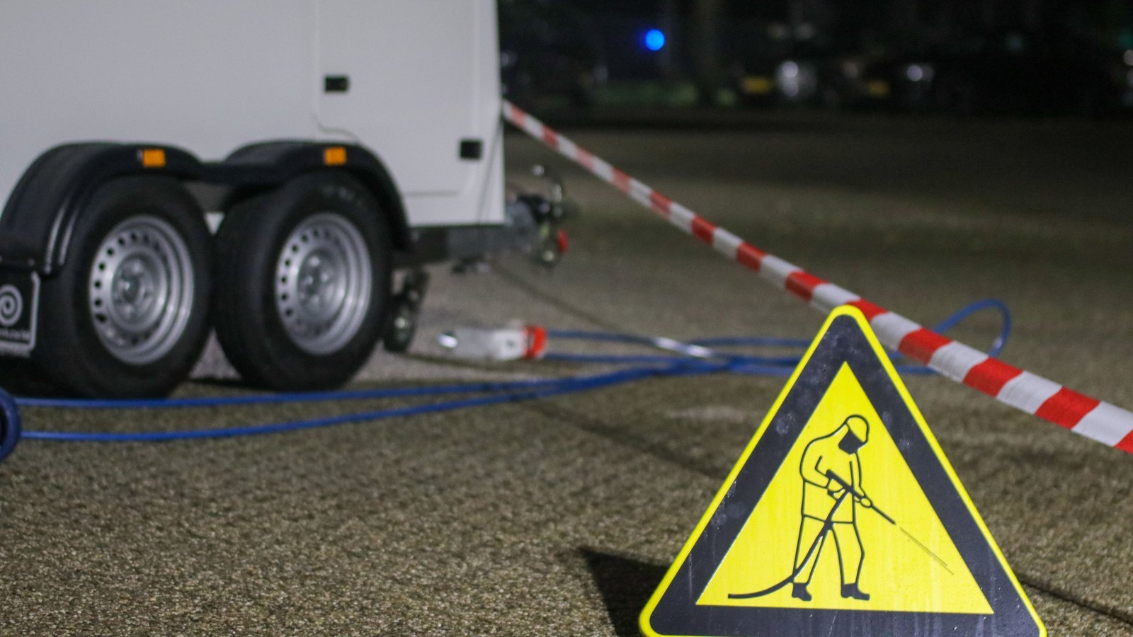 A triangular work zone warning sign beside red and white barrier tape at night, not a photograph of this event.