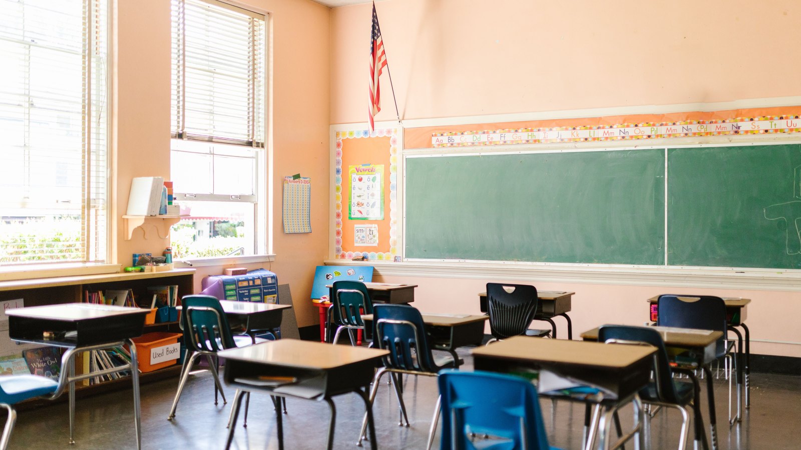 An empty classroom with student desks, a chalkboard and an American flag, not a photograph of a school in this report.
