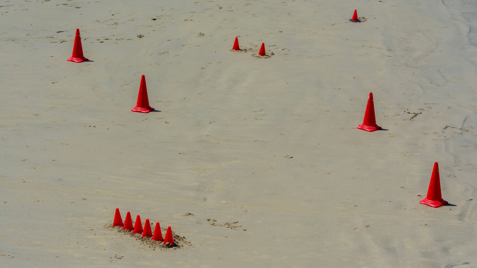 Red traffic cones stand across a sandy beach with no people, signs or identifiable location, not a photograph of these projects.