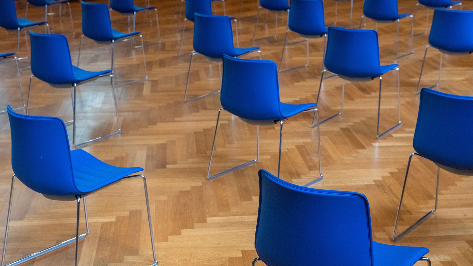 Empty blue chairs arranged in rows across a meeting room, not a photograph of this event.