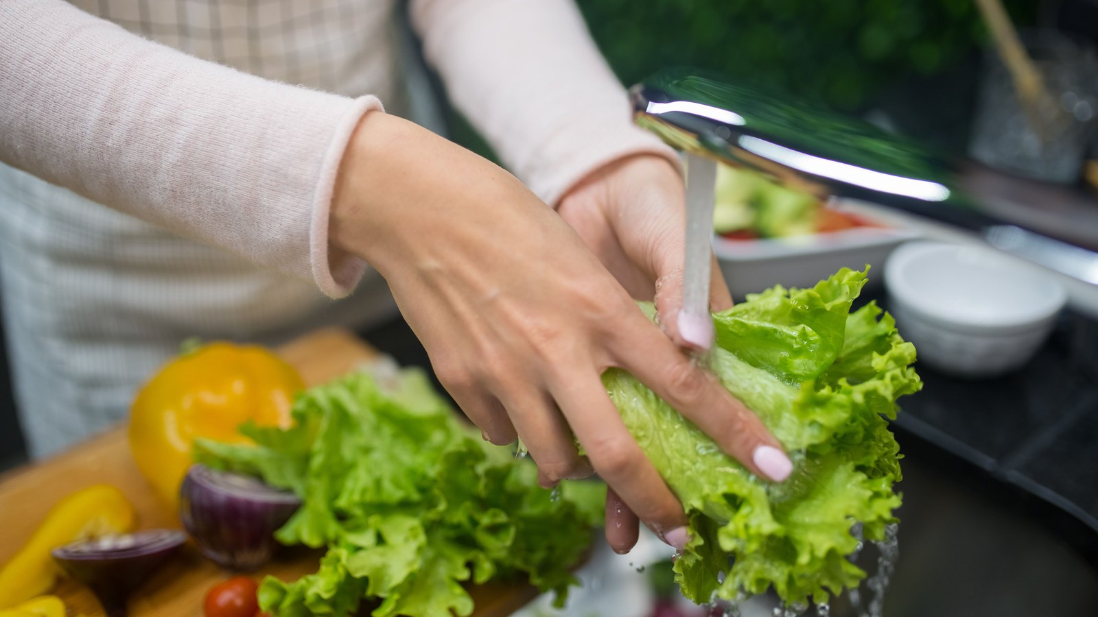 A photograph illustrating washing lettuce under kitchen tap.