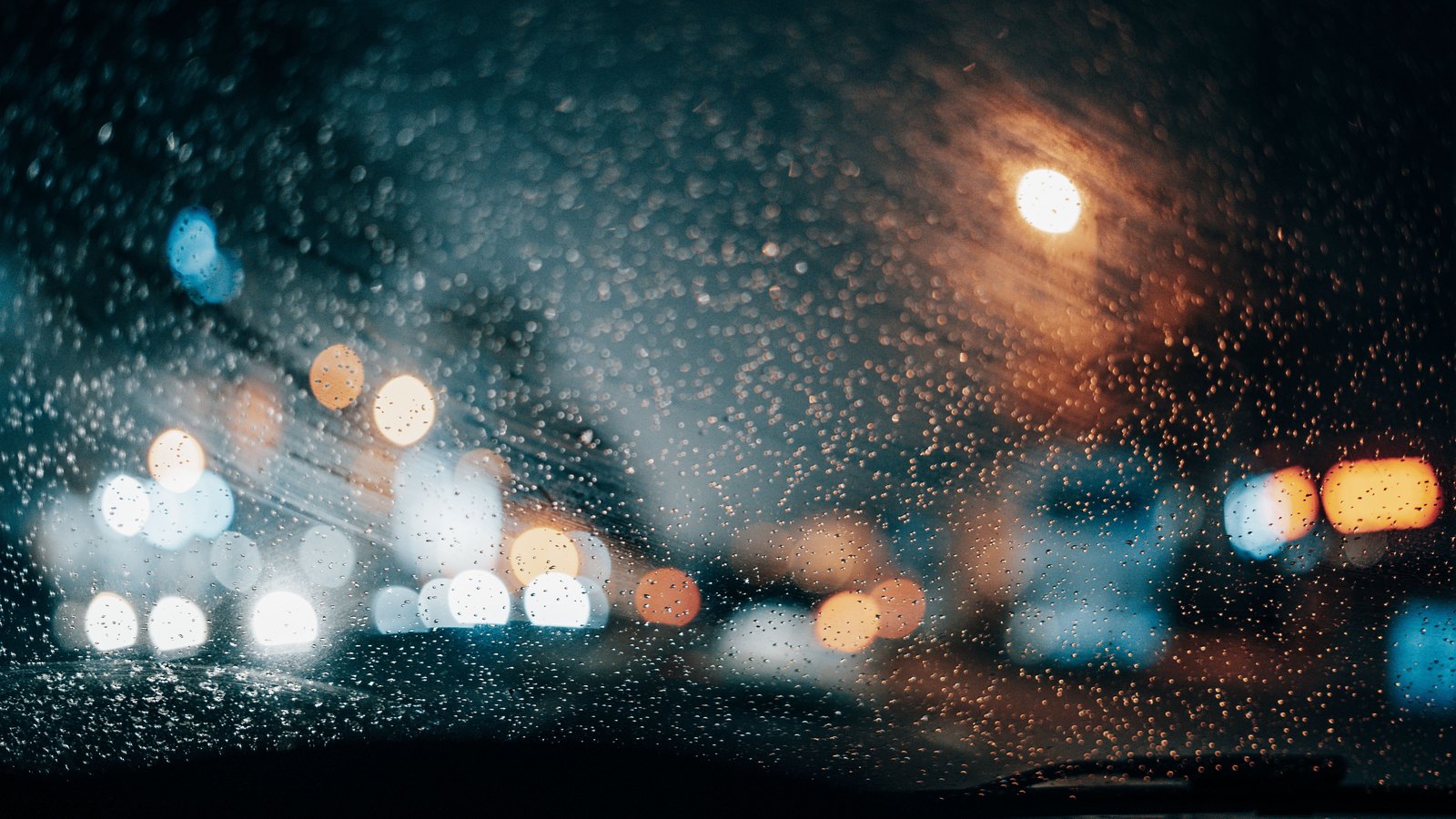 Rain beads on a windshield as lights blur on a dark street, not a photograph of this event.