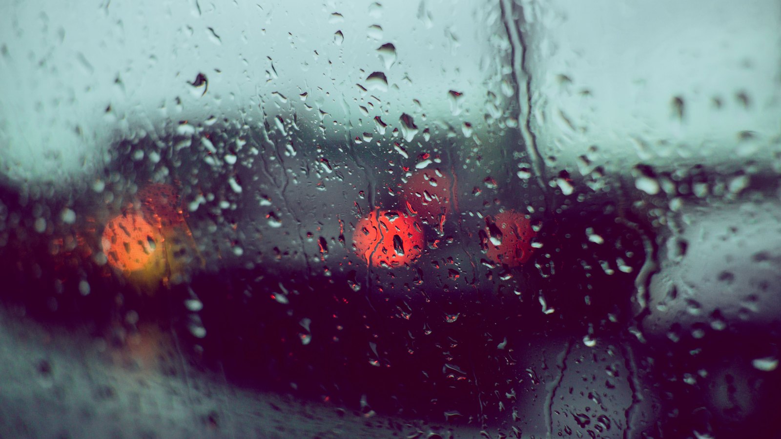 Rain beads on glass while red traffic lights blur beyond it, not a photograph of this advisory.