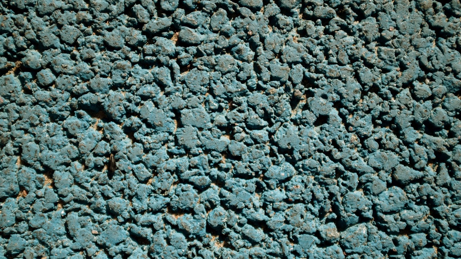 A close crop of coarse road aggregate, the loose grey stone chippings tinted blue green and packed edge to edge across the whole frame.