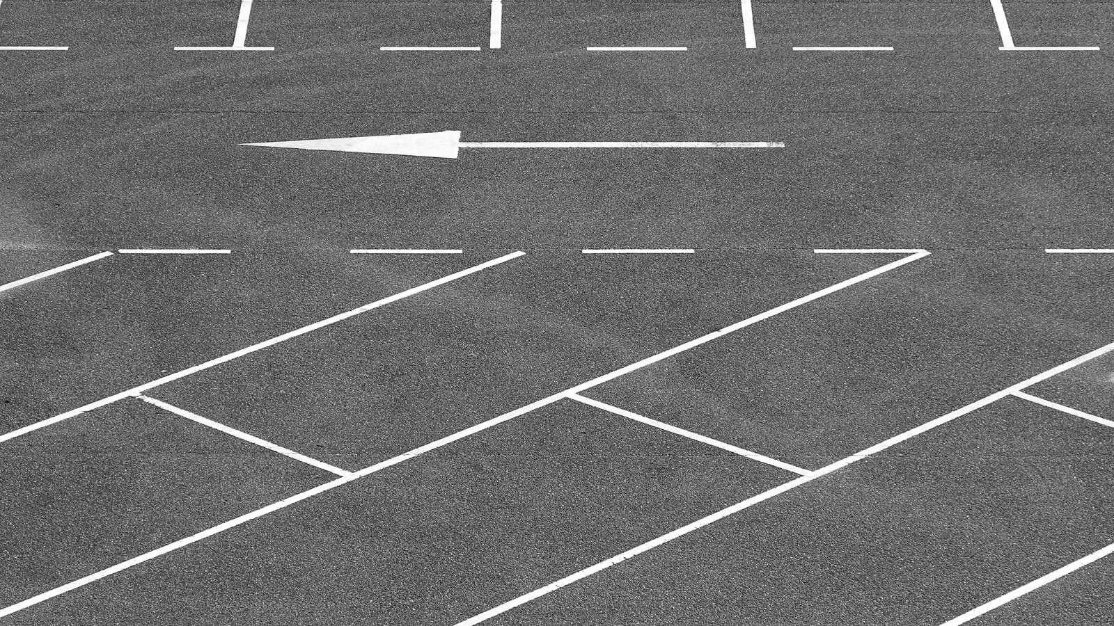An empty asphalt parking lot marked with white painted stall lines and a directional arrow, with no vehicles in any of the spaces.