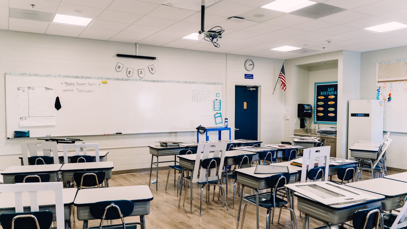 An empty classroom with rows of student desks, a whiteboard and an American flag, used as an illustrative image and not a photograph of the Lee County School Board meeting.