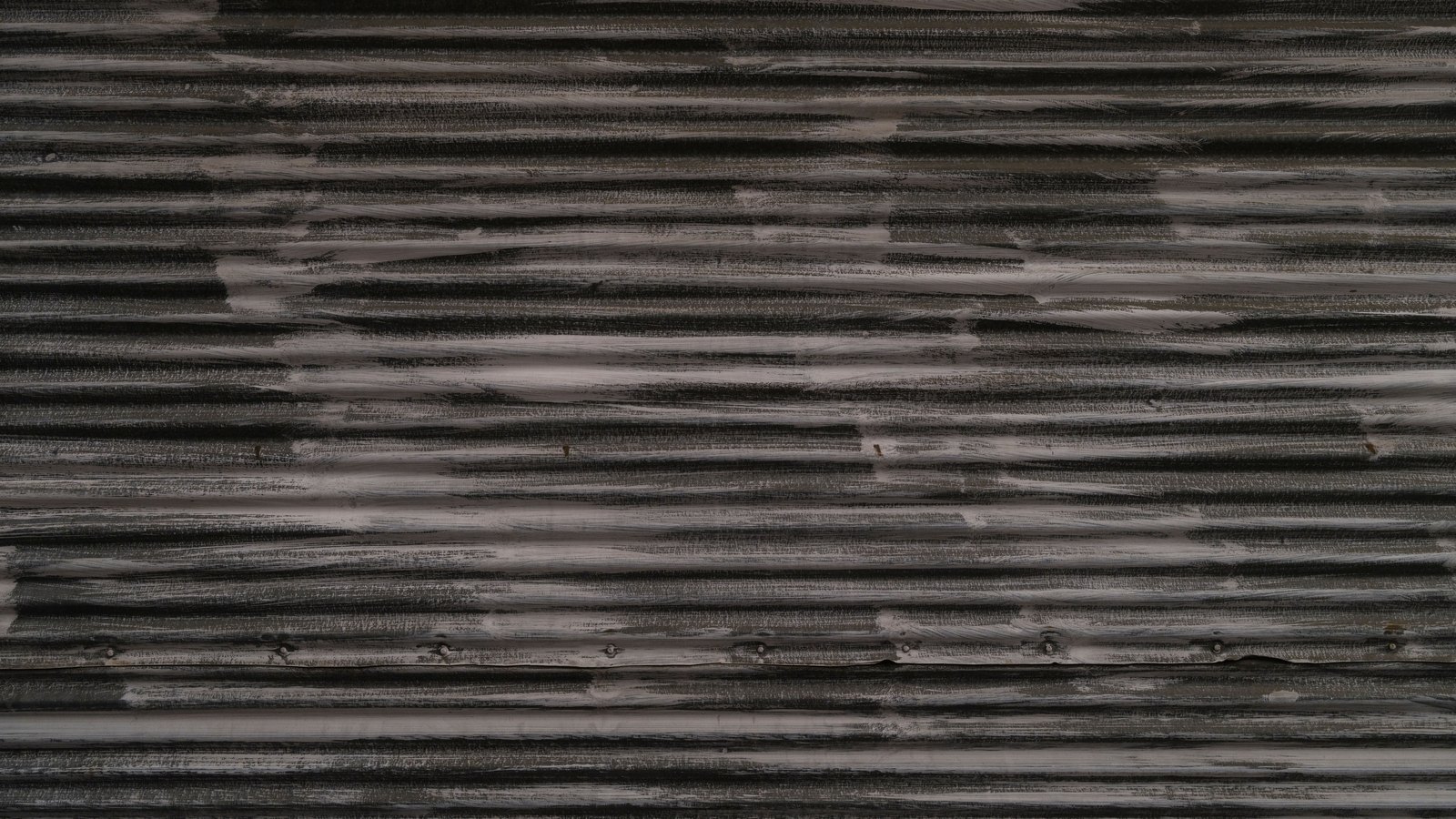 A close, straight-on crop of a weathered horizontally ribbed metal panel in dark grey, its raised edges rubbed to pale bare metal along their length. No lettering, badge, vehicle, person or place is visible. A generic metal texture, not a photograph of any Lee County building or vehicle.