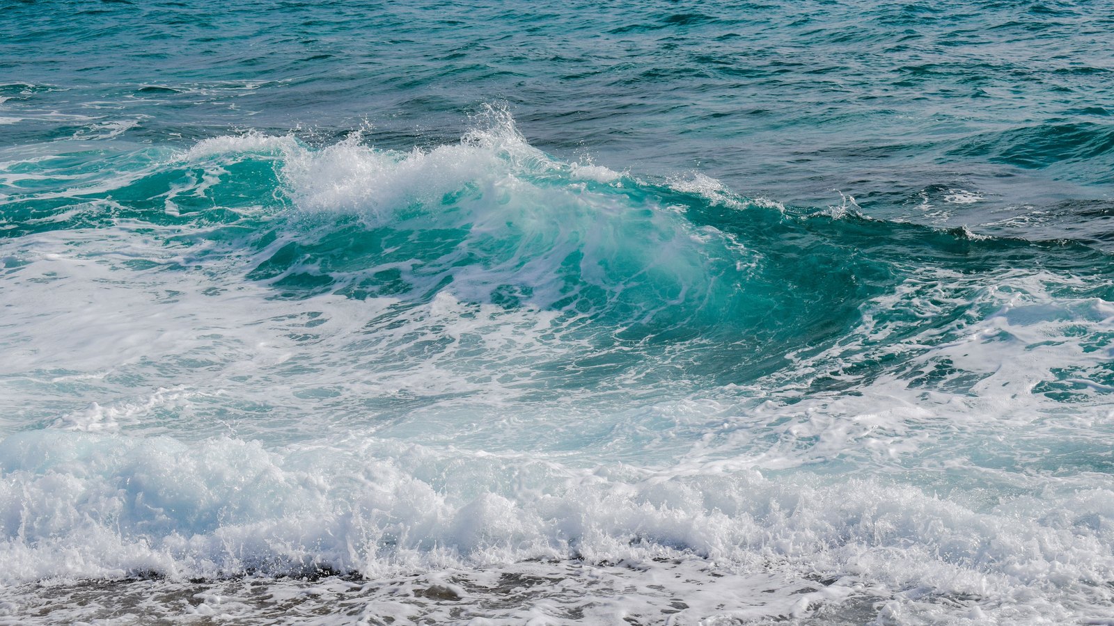 Large turquoise waves break toward a sandy shoreline in a generic weather photograph, not a photograph of these conditions.