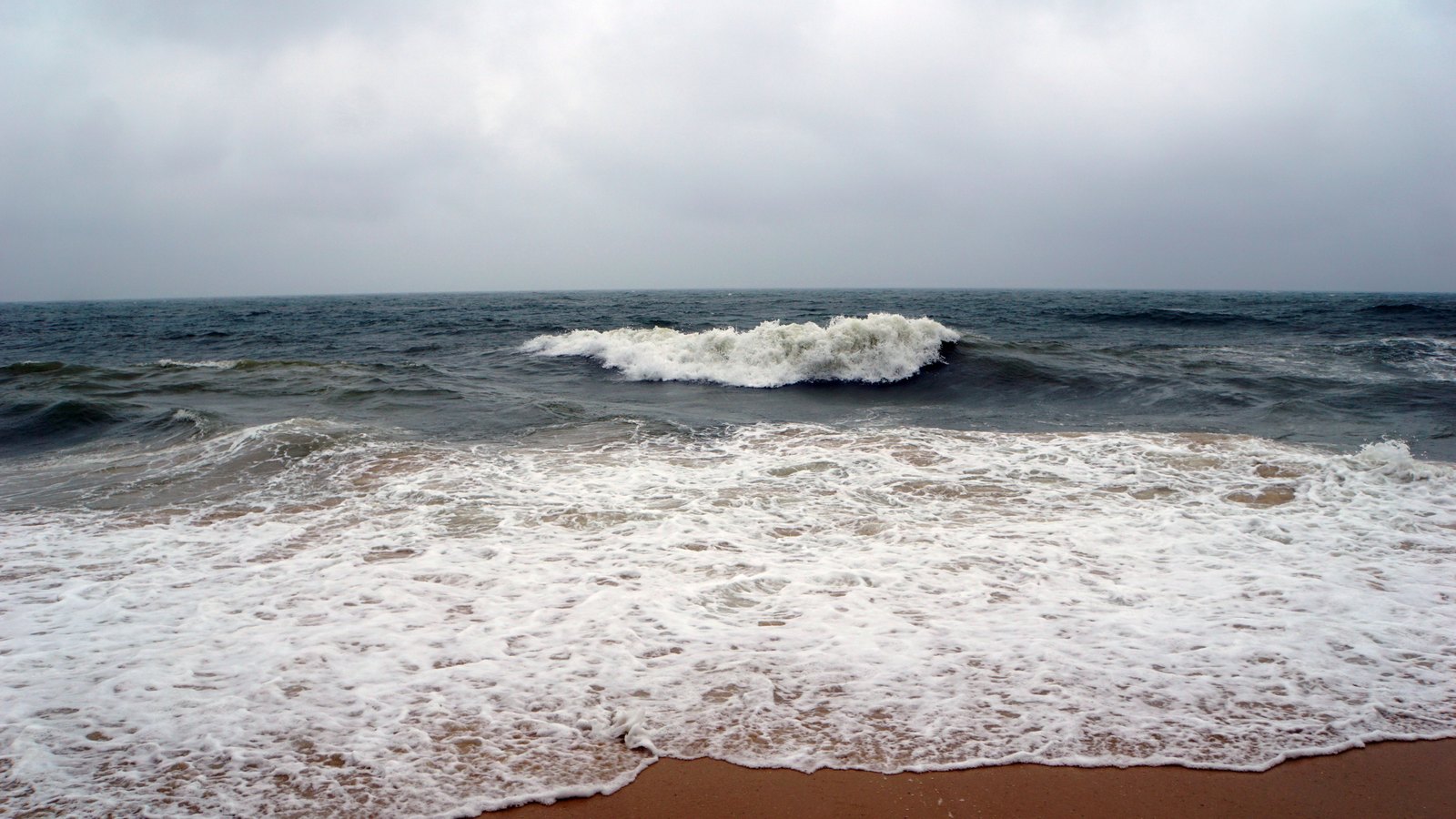 Rough waves break on an empty sandy beach beneath an overcast sky, not a photograph of these conditions.
