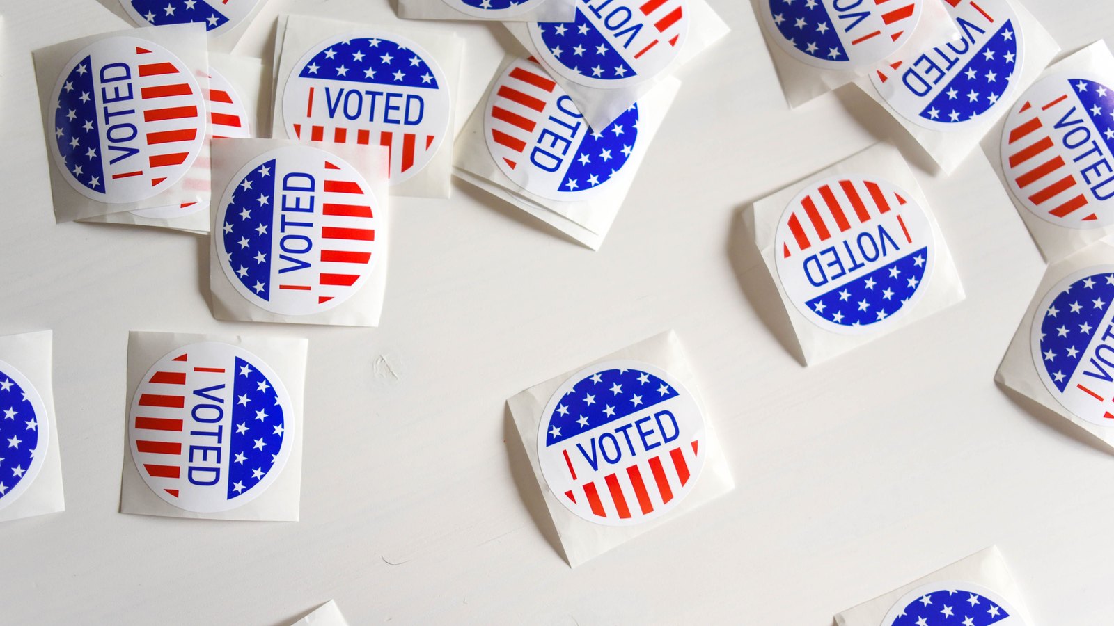 Round I Voted stickers printed with stars and stripes, scattered loose across a plain white surface, seen from above. No people, place or other lettering is visible. A generic election image, not a photograph of this event.
