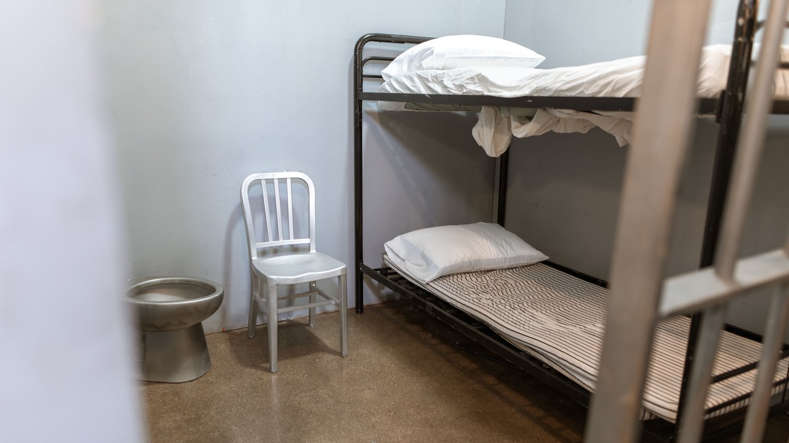 An empty generic detention cell with metal bunks and a chair, not a photograph of this event.
