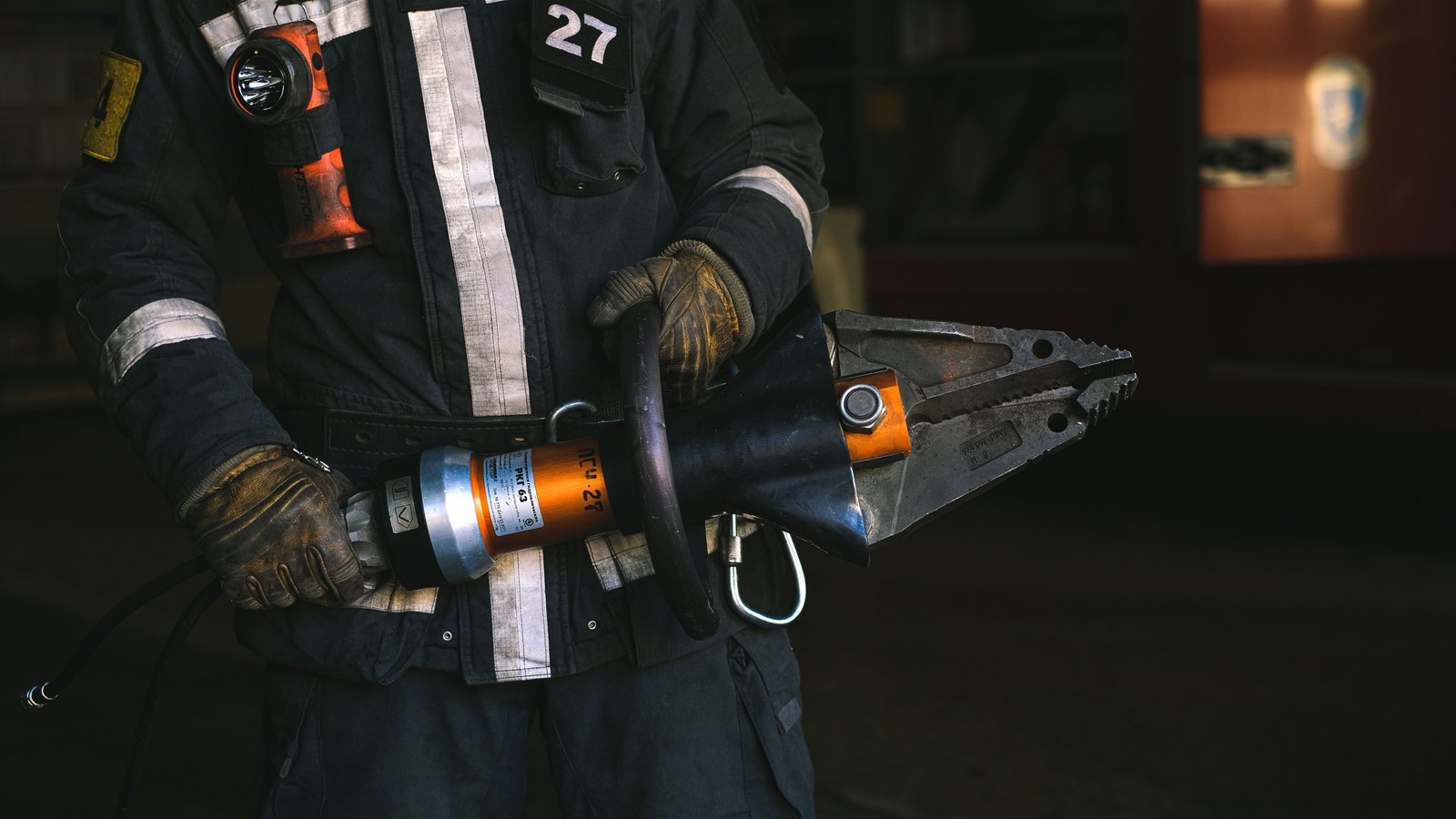 A firefighter in turnout gear holds a hydraulic rescue tool, not a photograph of this event.