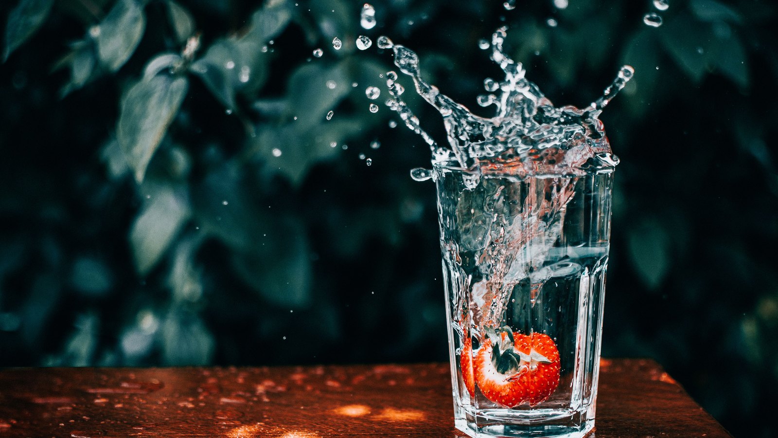Water splashes from a clear glass containing a strawberry on a wooden surface, not a photograph of this event.