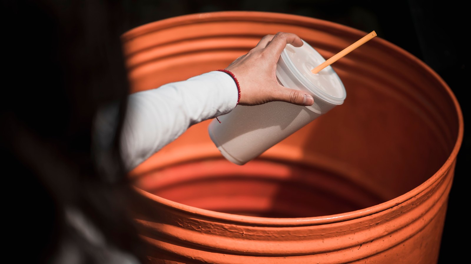A hand holds an unbranded drink cup over an orange waste bin, not a photograph of these collection routes.