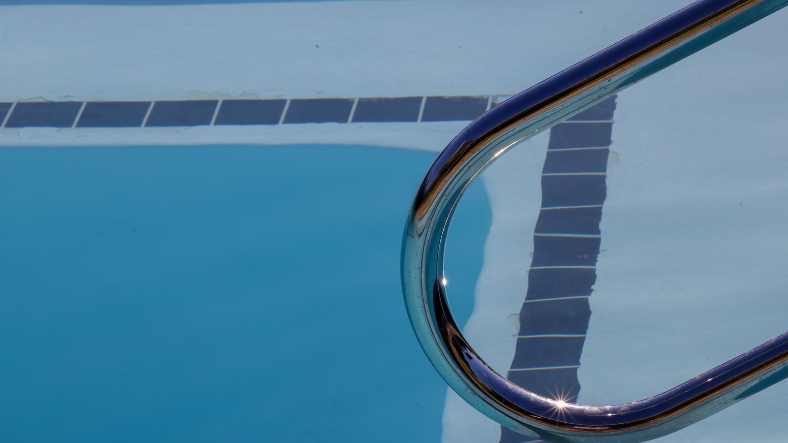 A stainless-steel handrail curves into a clear blue swimming pool.
