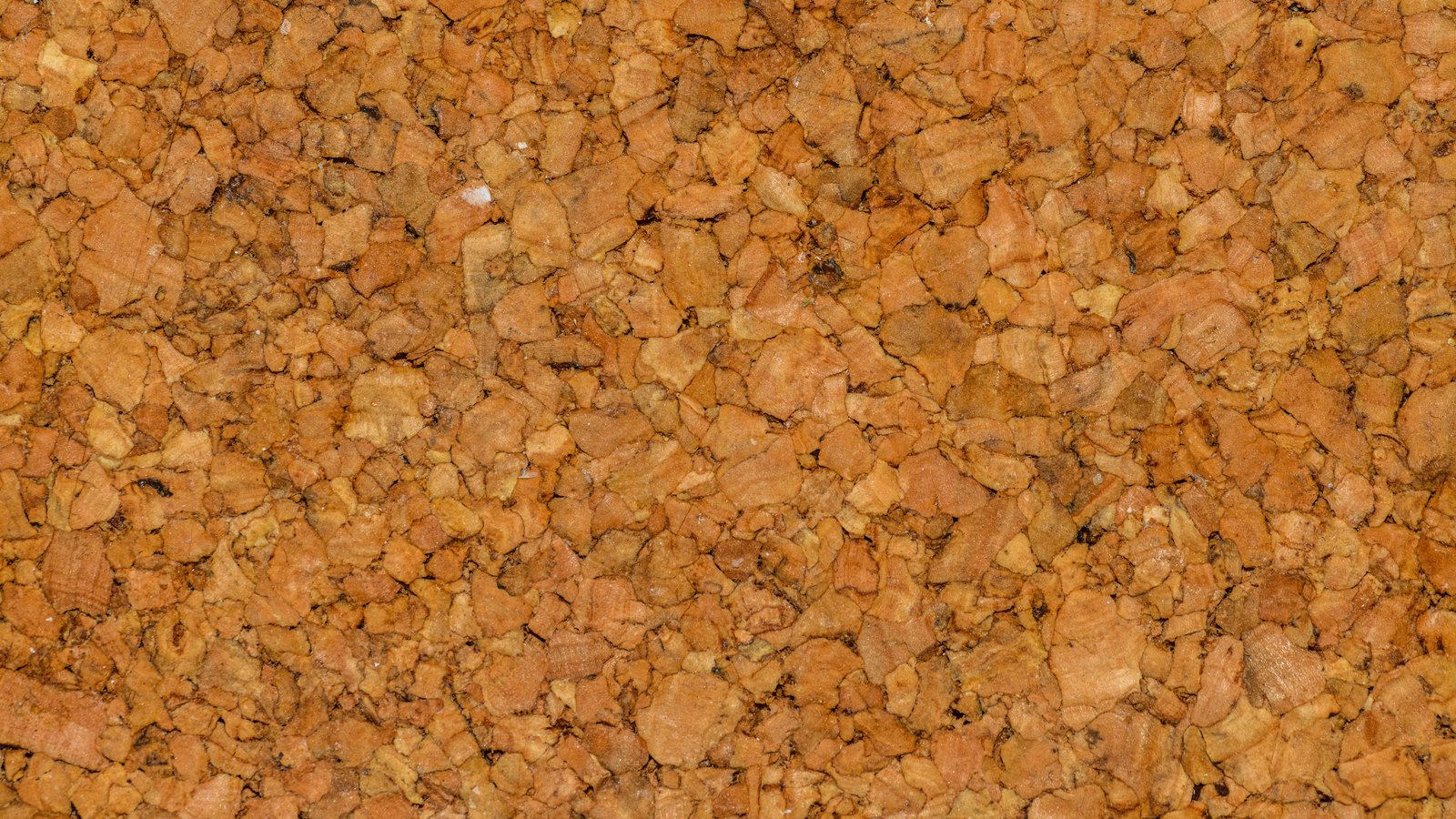 A close photograph of a pressed cork surface filling the frame, hundreds of irregular orange and tan granules bonded edge to edge, some pale and some darkened.