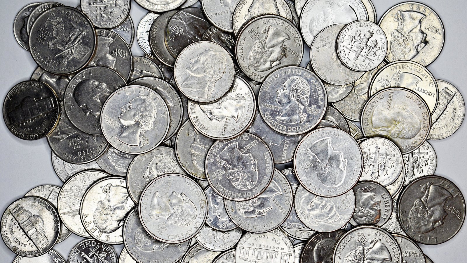 A dense heap of United States coins filling the frame, quarters, dimes and nickels lying face up and face down over one another, with the minted inscriptions visible on the faces. An illustrative photograph.