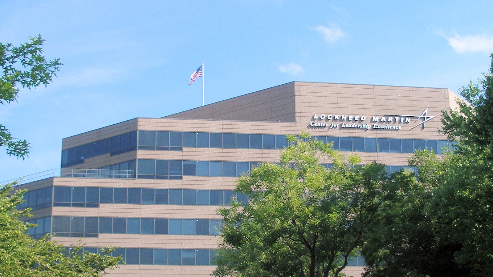 The upper storeys of a pale stone Lockheed Martin office building in Bethesda, Maryland, signed Center for Leadership Excellence, with an American flag on the roof and trees in front.