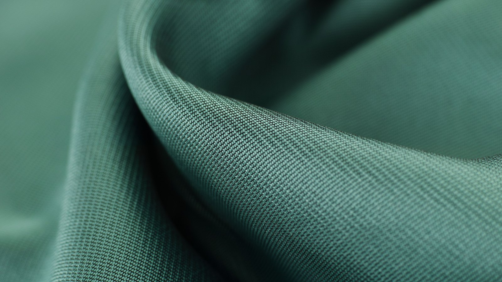 A close photograph of finely woven green satin cloth folded into soft curves, the weave visible where the light falls across the fold.