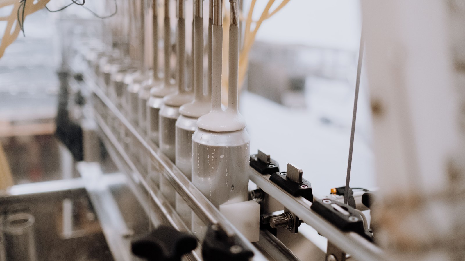 Metal nozzles fill a row of unlabelled cans on an automated production line