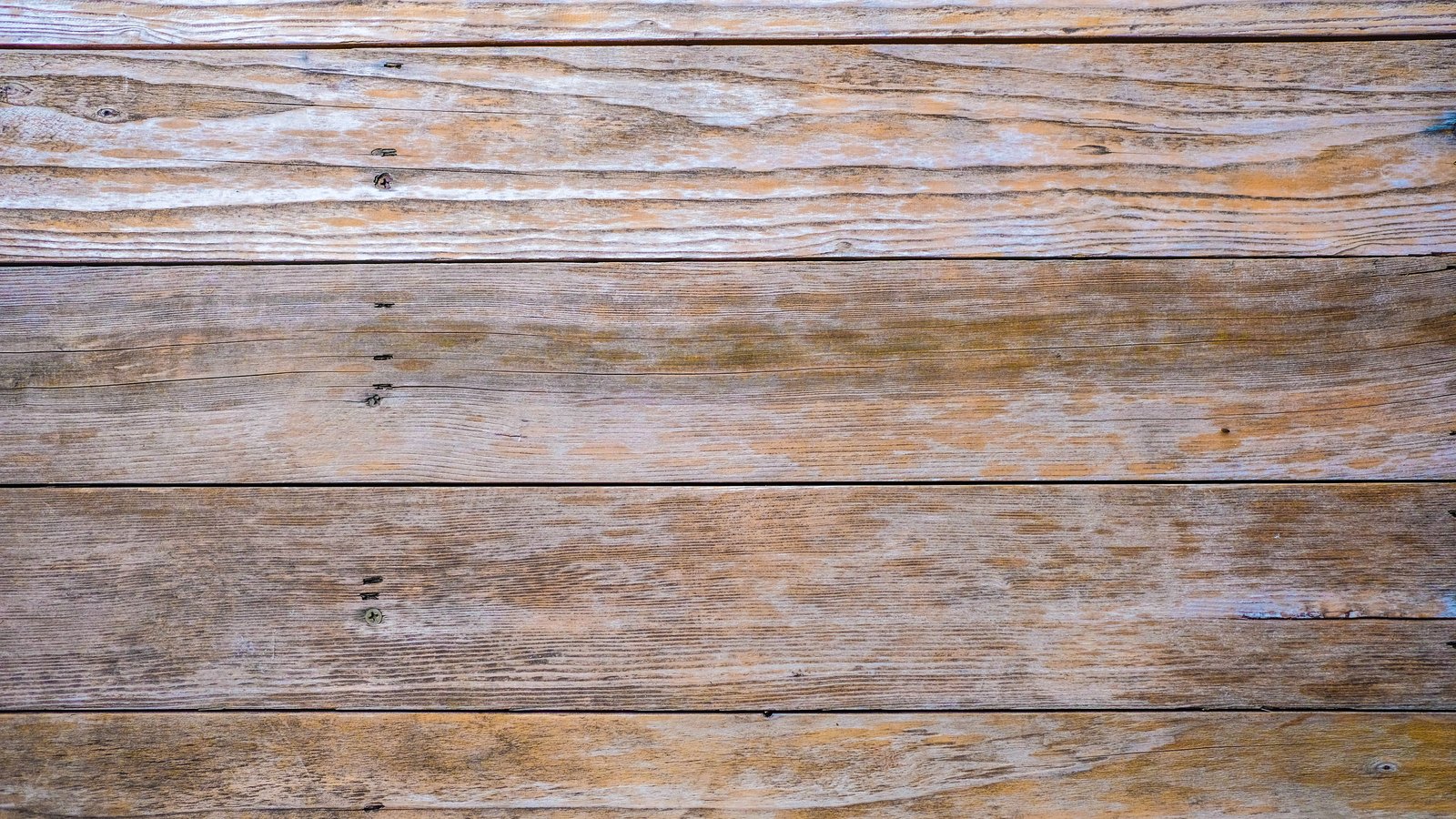 A flat overhead photograph of five weathered horizontal wooden planks, greyed and sun bleached with visible grain, a few small screw heads and rust coloured staining. No people, no lettering, no signage and no place can be identified from it. A neutral surface texture used as an abstract illustration, not a photograph of Marco Island, its city hall or its police department.