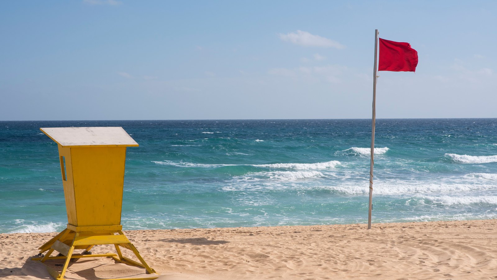 A red warning flag and an empty lifeguard station beside ocean surf, not a photograph of this advisory.