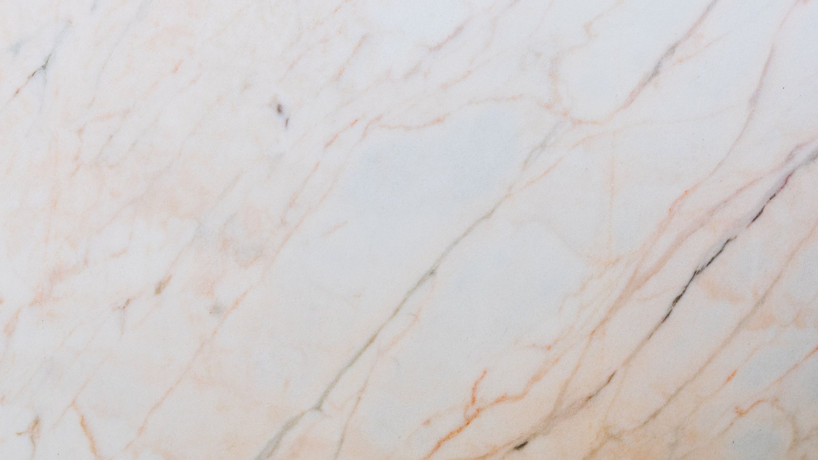 A close photograph of a polished slab of pale marble, filling the frame. Fine ochre and grey veins run diagonally across a cream and off-white ground, branching and thinning toward the corners. No object, person, lettering or brand mark is in the frame.