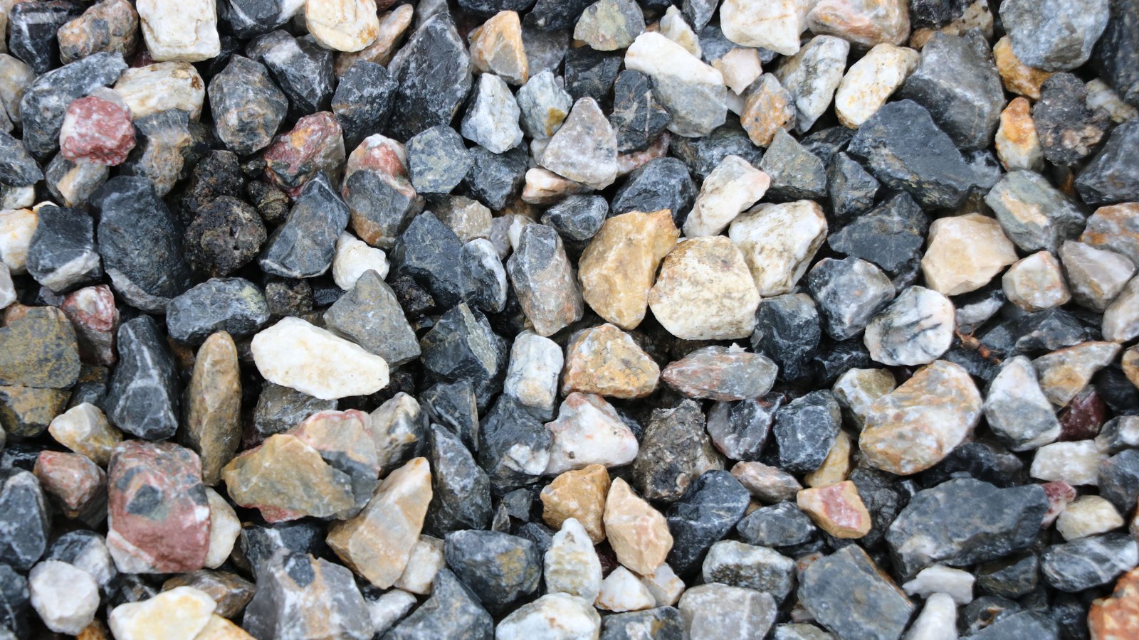 Crushed stone aggregate filling the frame, angular grey, white and tan fragments of varying size packed tightly together.