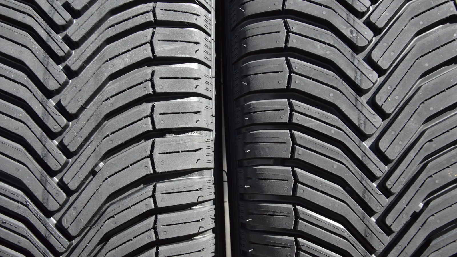 Two new black car tyres standing side by side, cropped so that their deep chevron tread blocks fill the whole frame. No brand name, logo, wheel or background is visible.