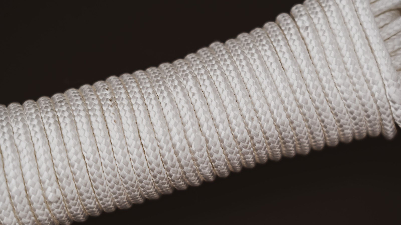 A close photograph of white braided nylon rope wound tightly into a coil against a plain dark background, filling the frame, with no text, people or setting in view.